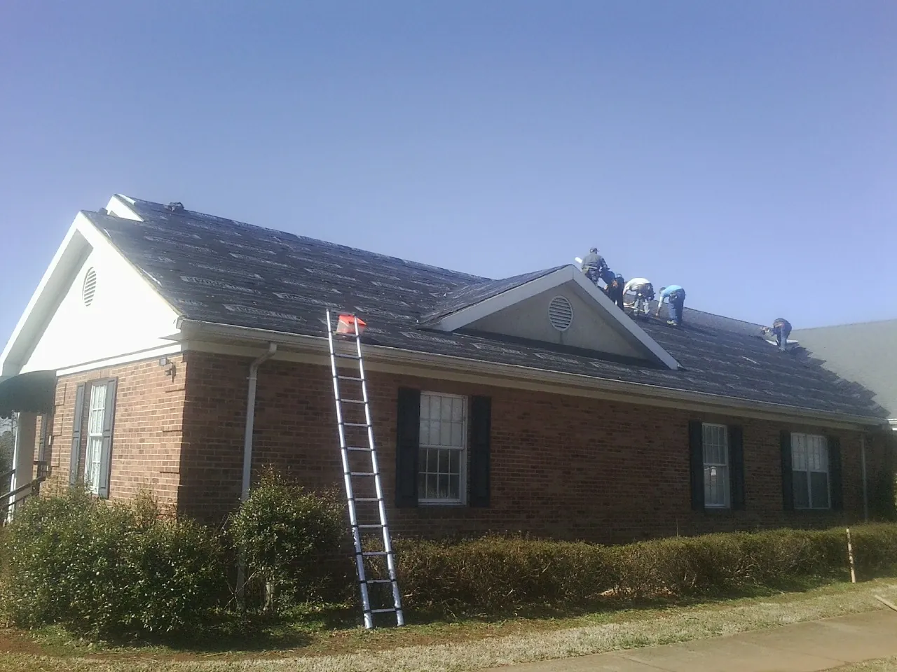 Crew tearing shingles off a brick ranch roof with a ladder set — Emergency Roof Repair work by our crew in Charlemont