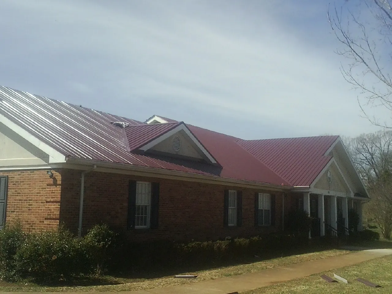 Red metal roof with gabled entries on a long brick building, from a Hail Damage Roof Repair job in Charlemont