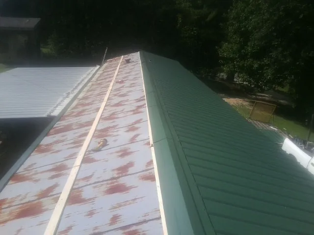 Old rusted panels beside newly installed green metal roofing — Wind Damage Roof Repair by Roofing Brothers in Charlemont