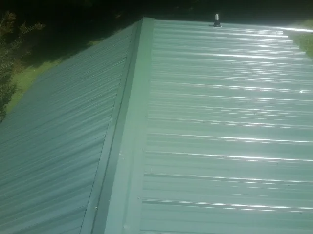New green metal panels meeting at the ridge of a roof — Flat Roof Repair work by our crew in Charlemont
