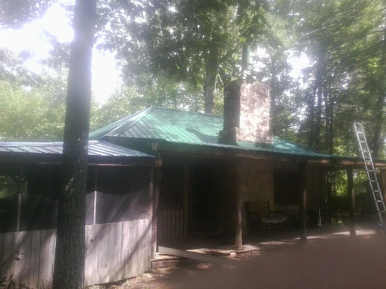 Green metal roof and stone chimney above a log cabin porch in Charlemont
