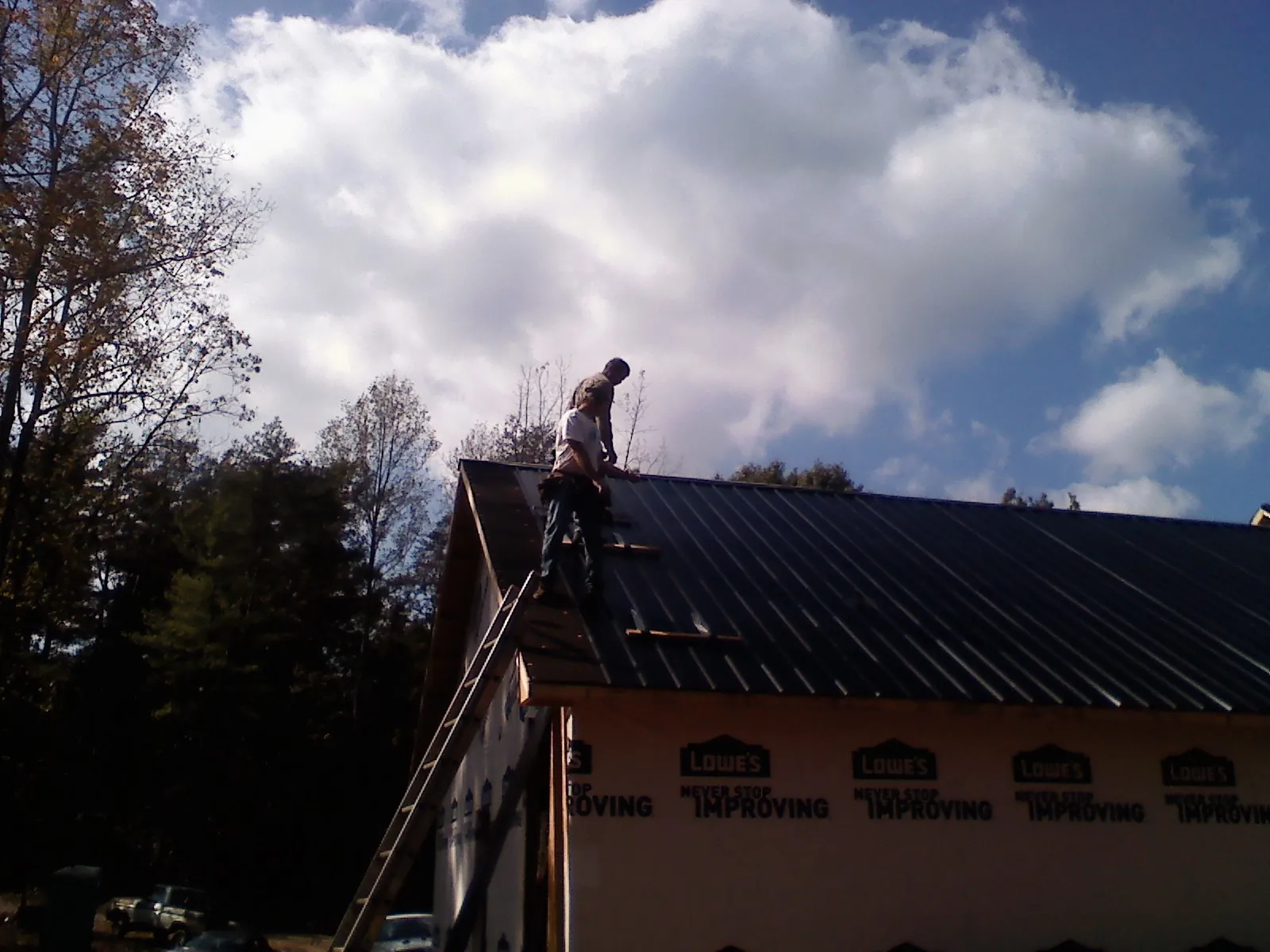 Roofer fastening dark metal panels high against a cloudy sky, from a Roof Inspection job in Charlemont