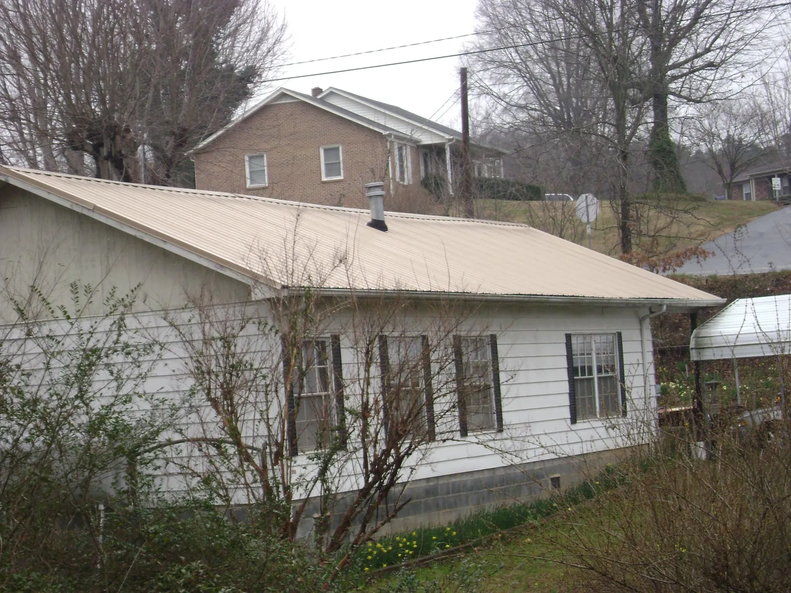 Tan metal roof on a white sided house set into a hillside — Commercial Roofing by Roofing Brothers in Charlemont