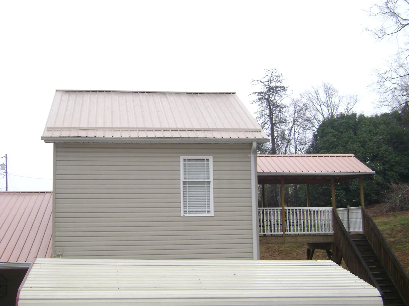Tan metal roofs on a two story addition and attached porch, from a Roof Replacement job in Charlemont